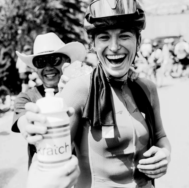 A rider laughing as she holds out a Skratch Labs bottle after finishing